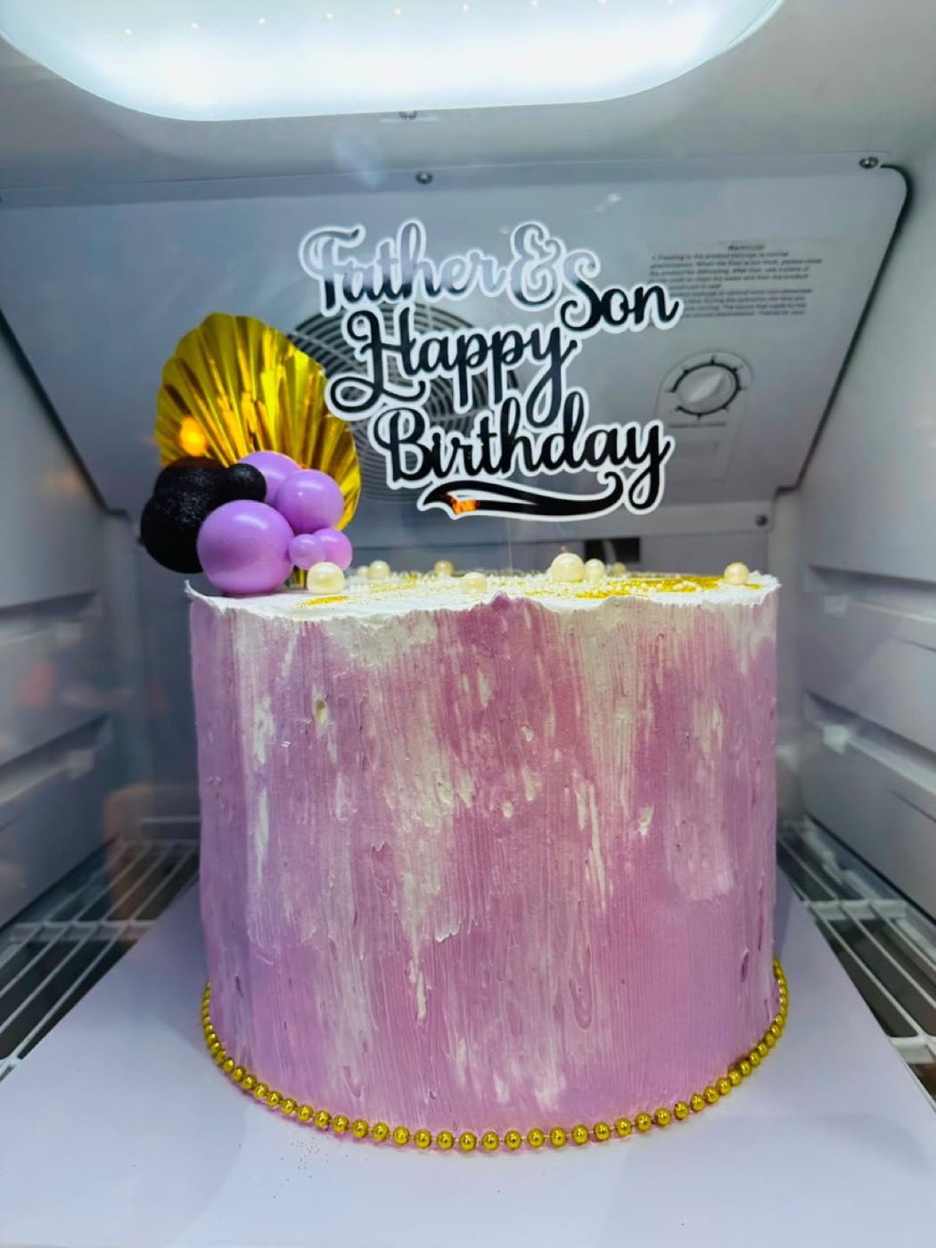A pink marbled birthday cake with gold decorations